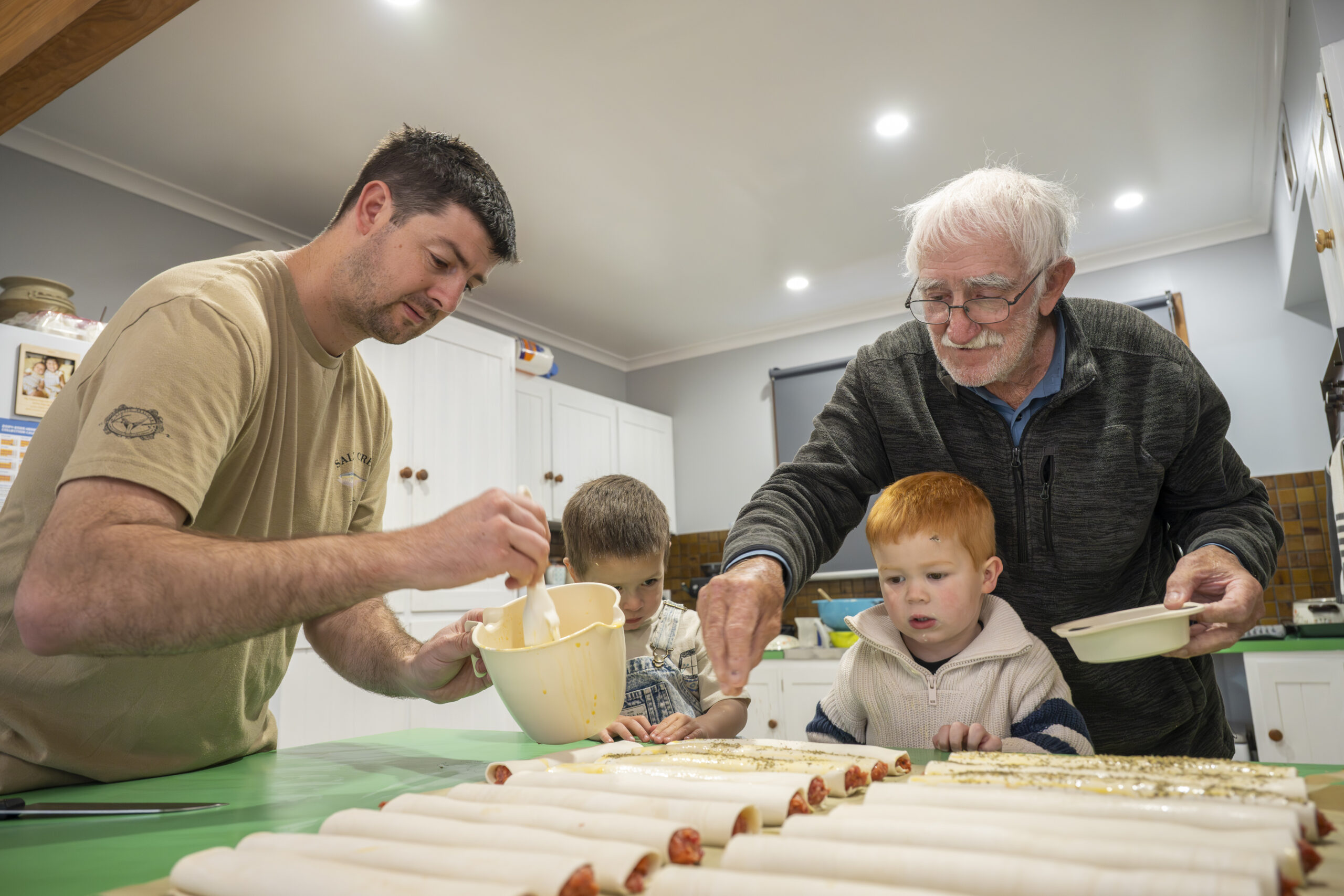 Lloyd Collins making sausage rolls with his grandson and great-grandchildren using his pastry rolling machine in Crystal Brook.